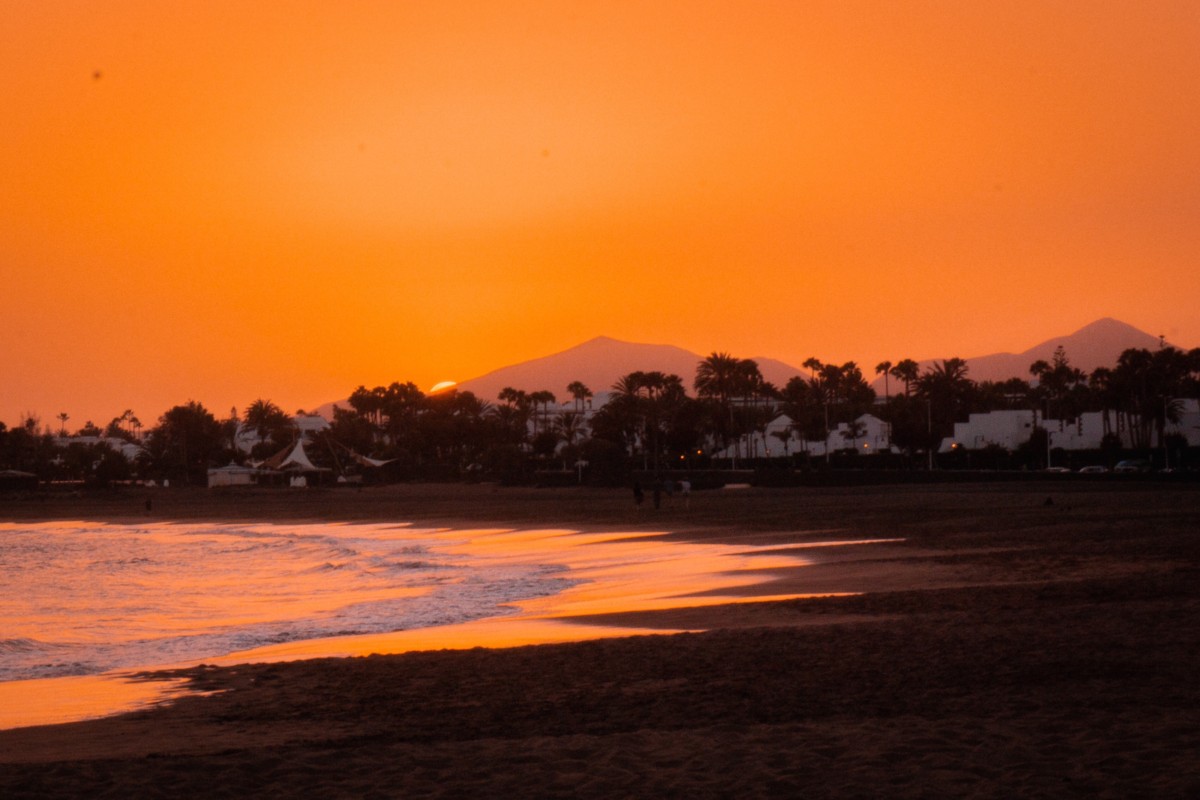 an orange sunset over the mountains and beach of puerto del carmen in Lanzarote